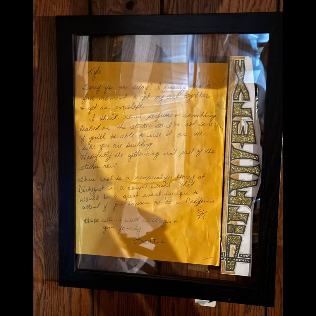 Framed handwritten yellow letter from Dottie Ellis-Merki displayed beside a tall DIRTWERX decal.