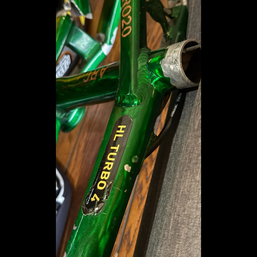 Close-up of a metallic green BMX frame marked HL TURBO 4, showing wear and damage near the bottom bracket.