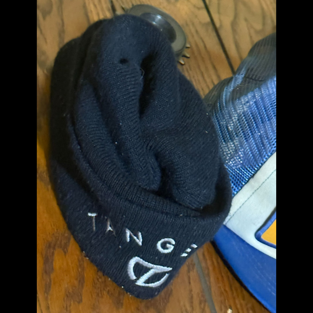 Worn dark Tangent beanie photographed beside another hat on a wood floor.