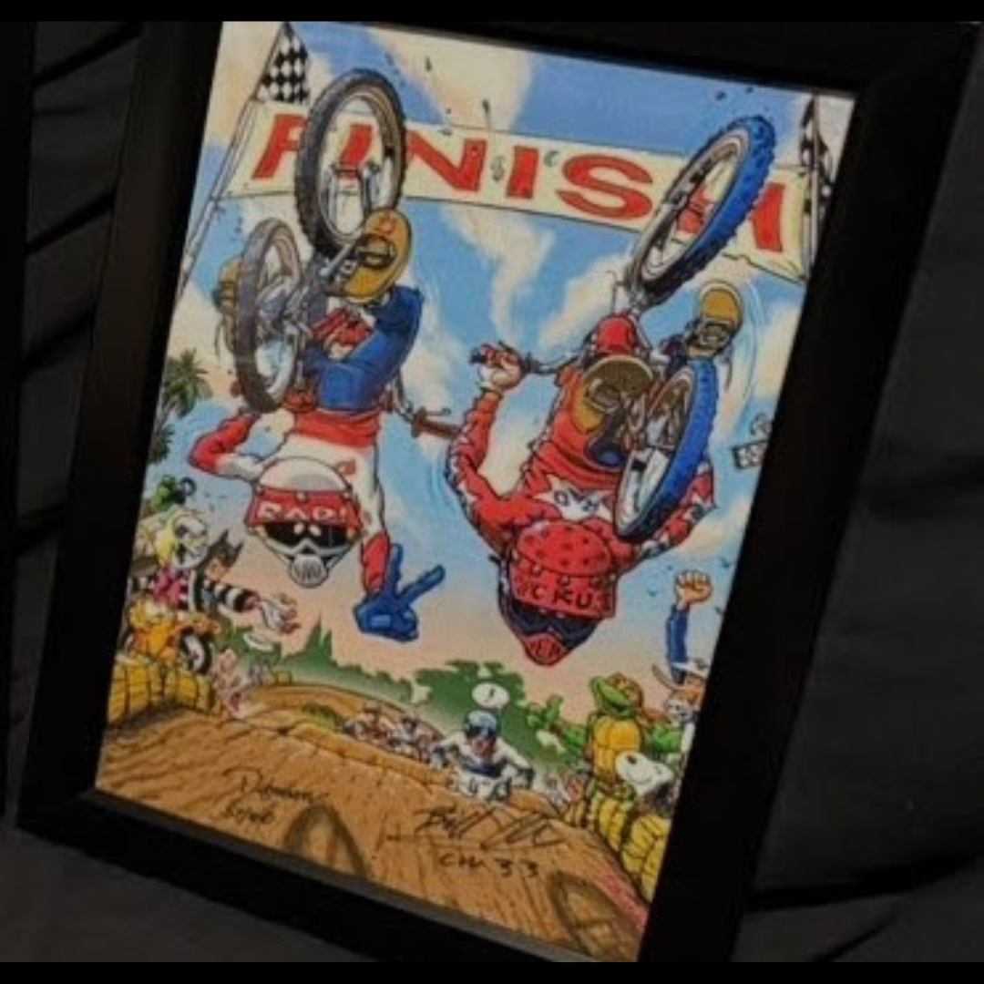 Framed print showing two BMX riders upside down near a finish banner, with signatures visible along the lower edge.