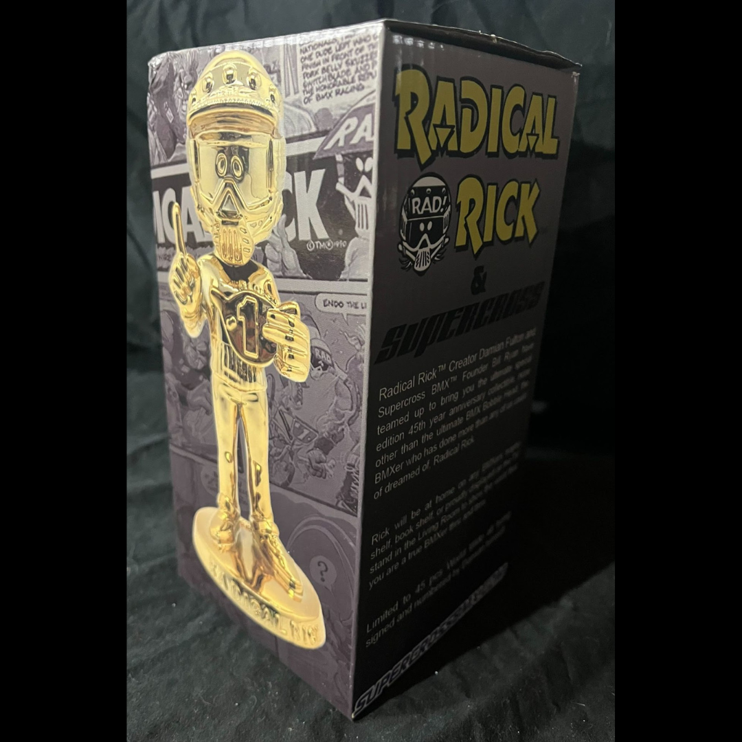 Boxed gold Radical Rick Supercross bobblehead with comic-panel graphics and product text on the package.