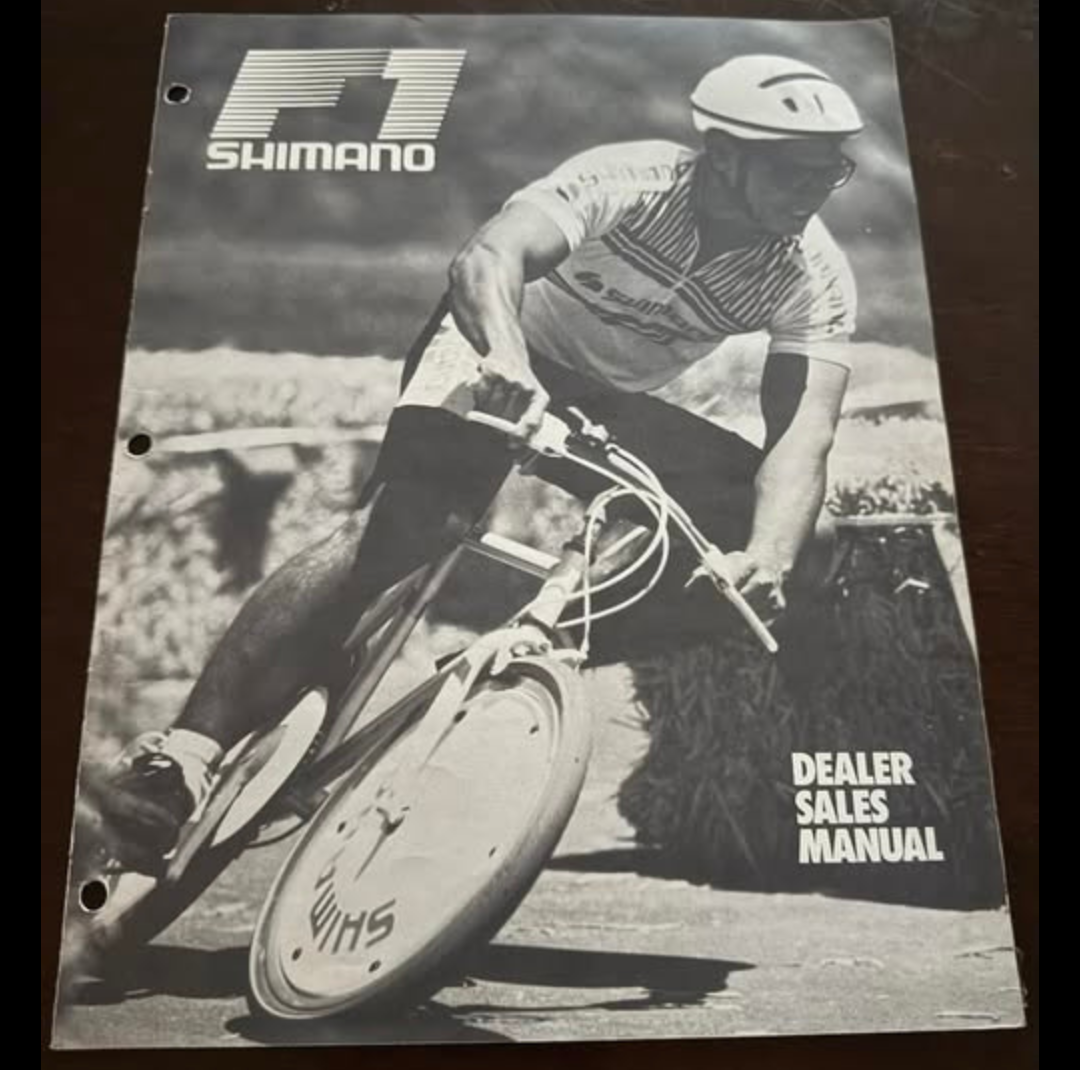 Vintage Shimano dealer sales manual featuring a helmeted cyclist leaning a bicycle into a turn